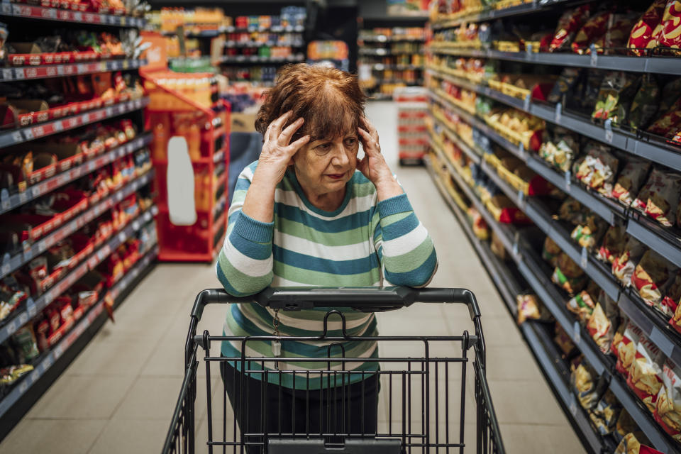 Elderly woman standing in supermarket produce aisle and worried about rising grocery prices