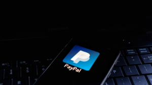 PayPal Holdings, Inc. (PYPL) icon displayed on smartphone with keyboard background.  is an American multinational financial technology company that handles online payments