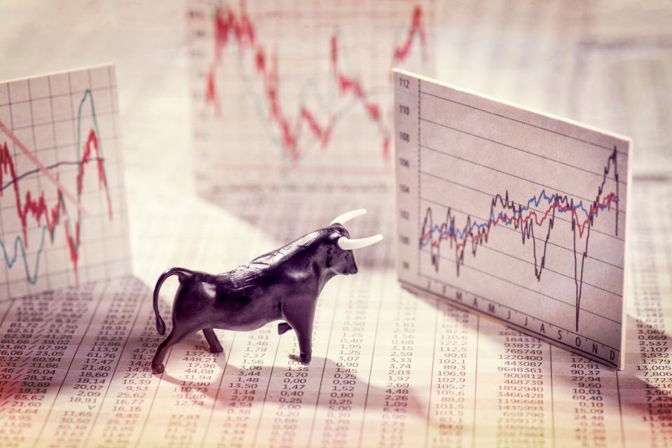 A bull figurine placed on top of a financial newspaper and in front of a volatile but rising pop-up stock chart.