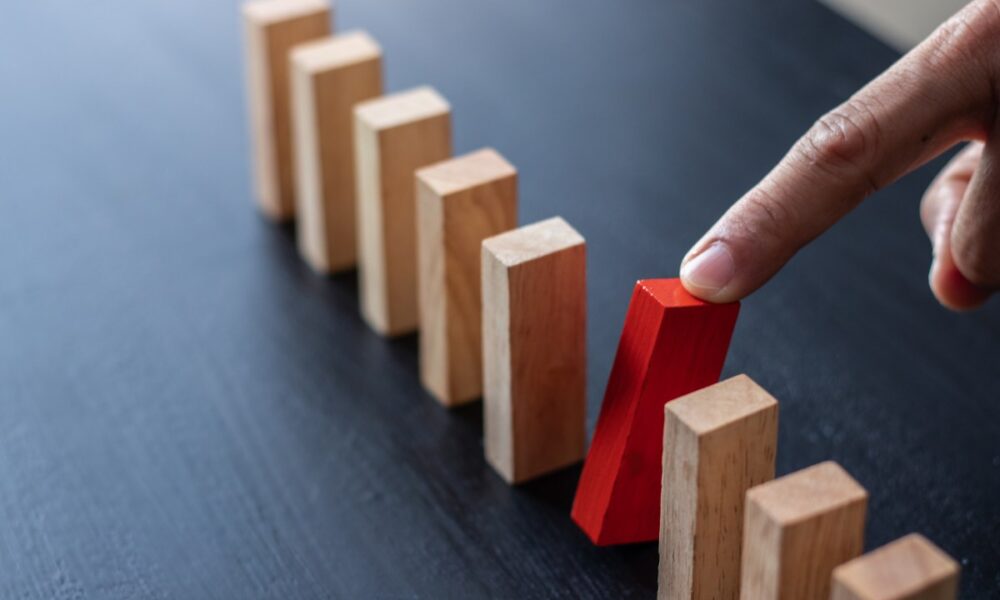 finger pulling red domino block out of row of dominoes