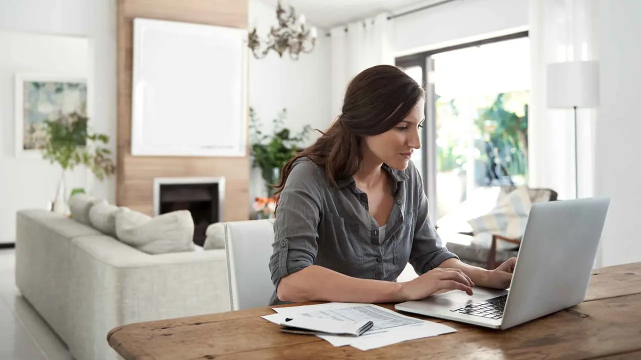 Shot of woman using laptop while completing paperwork at home.