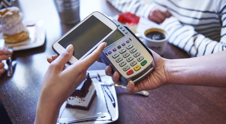 a person holding a smartphone over a check out scanner representing payments stocks to buy