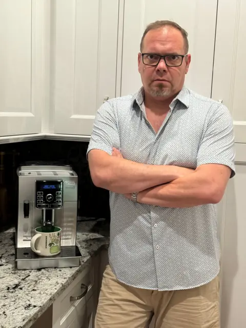 Andrew Buckley Andrew Buckley standing with his arms crossed in his kitchen next to his coffee machine