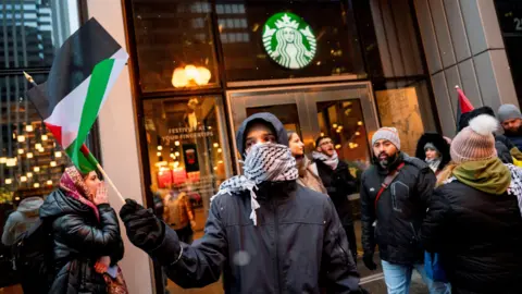 Getty Images Activists from the group Chicago Youth Liberation for Palestine protest outside a Starbucks in Chicago holding Palestinian flags