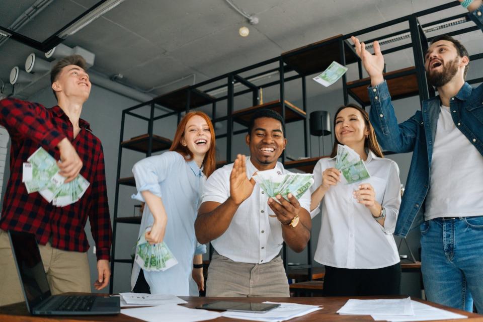 A group of five smiling people with handfuls of money.