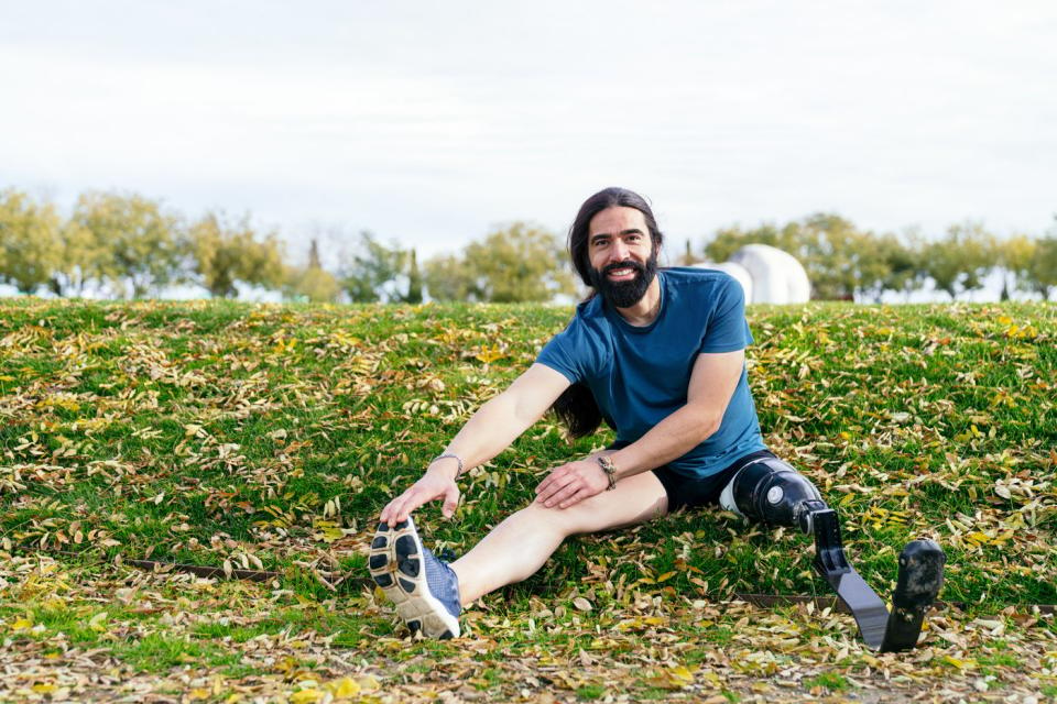 Someone smiles while sitting and stretching in a grassy area. 