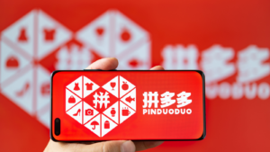 Man holding a cell phone with PinDuoDuo (PDD) logo in horizontal composition.