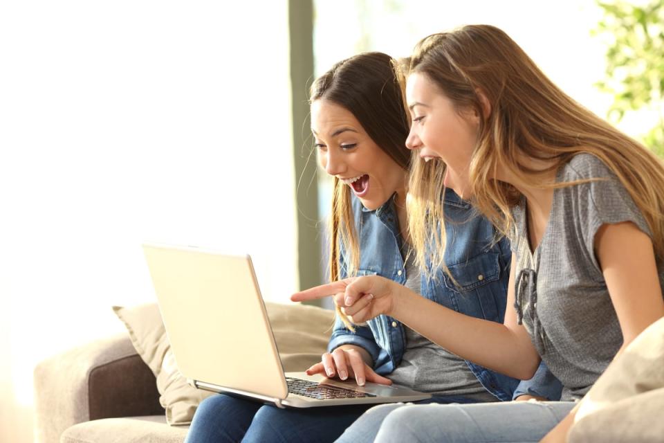 Two people smile while sitting on a sofa and point at a laptop.