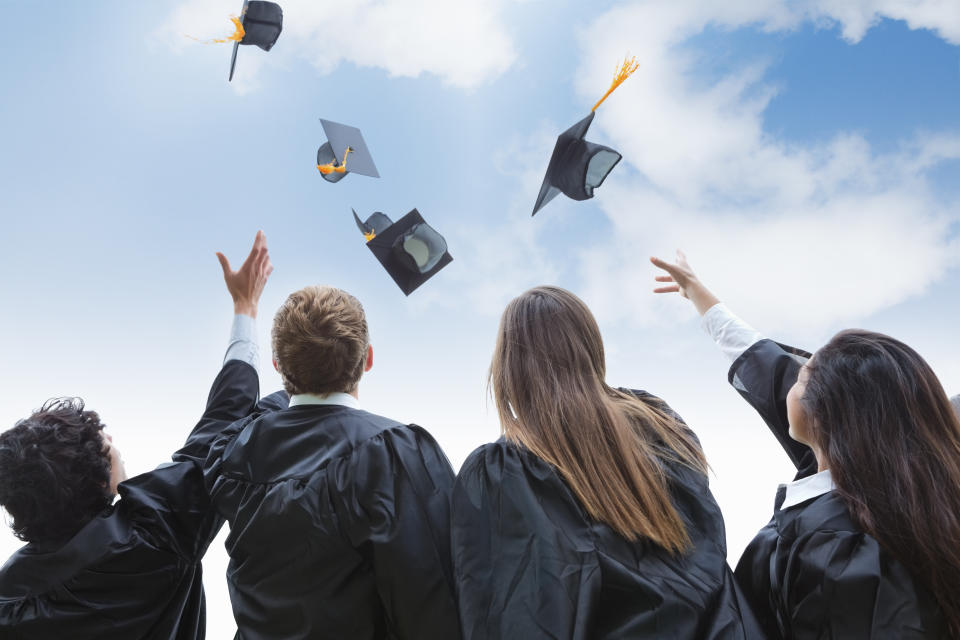 Grupo animado de graduados universitários jogando seus chapéus em comemoração