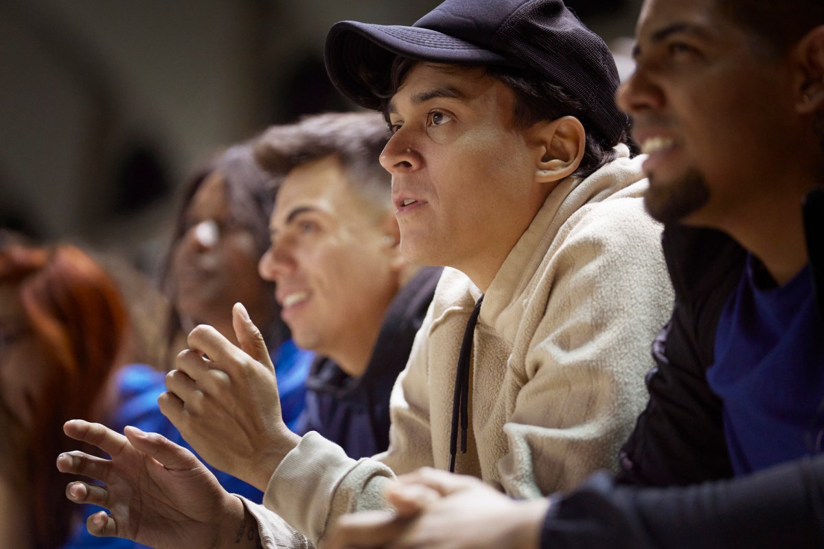 A young man anxiously watches a sporting event surrounded by a crowd of supporters all looking at a field. (Image Credits: Lighthouse Films/Getty Images)