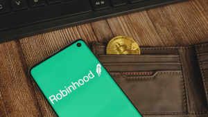 hood stock: An image of a wallet with a coin inside, a cell phone on top depicting the Robinhood logo. Robinhood crypto