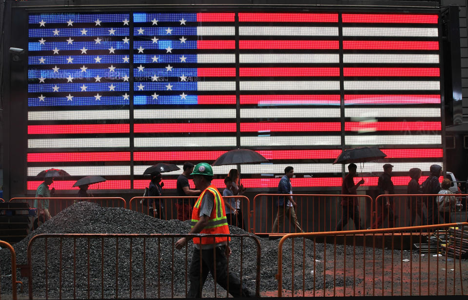 NEW YORK, NY - AUGUST 22: Pedestrians and a construction worker walk past a lit American flag in the rain in Times Square on August 22, 2013 in New York City. The afternoon rain that fell in the city today is expected to clear by tomorrow. (Photo by Mario Tama/Getty Images)